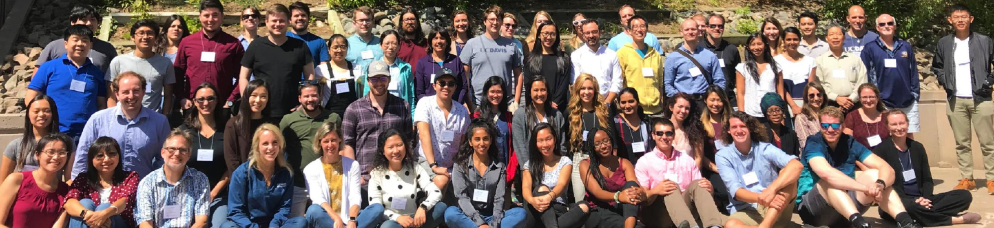 Large outdoor group photo of about 70 diverse adults smiling in front of trees.